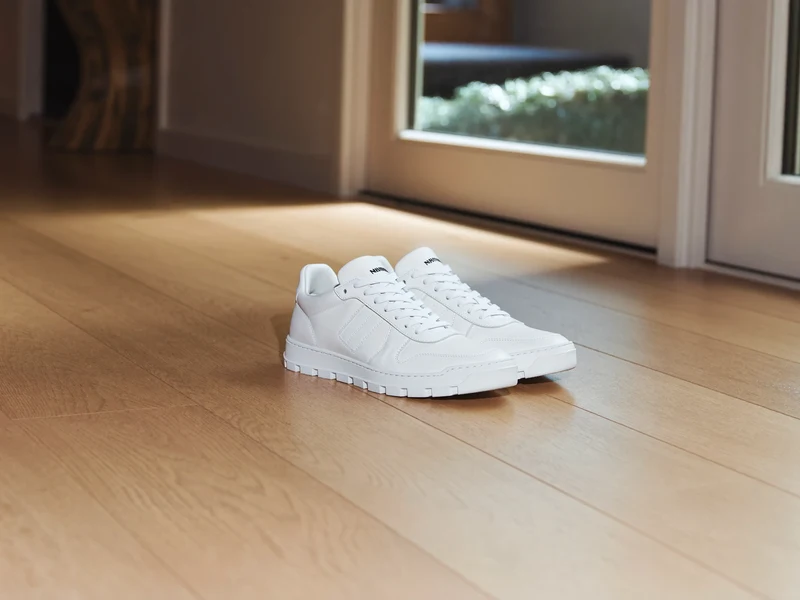 Saubere Sneaker auf hellem Eichenboden neben einem Fenster mit weichem Morgenlicht