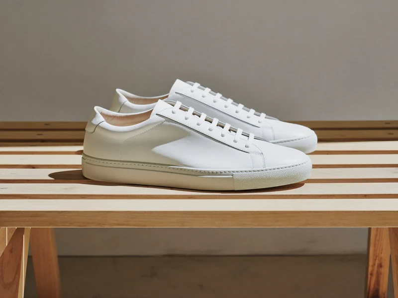 Weisse Low-Top-Sneaker aus Leder auf einer hellen Holzbank in Dreiviertelansicht