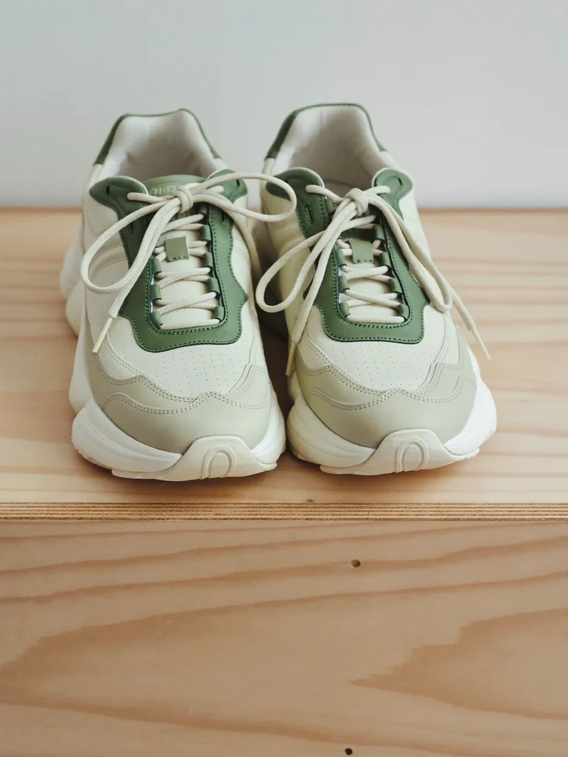 Off-White-Sneaker mit Salbeigrün und kräftiger Sohle auf einer Stufe aus Birkensperrholz